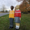 Two child-shaped bollards on grass by road