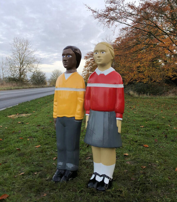 Two child-shaped bollards on grass by road